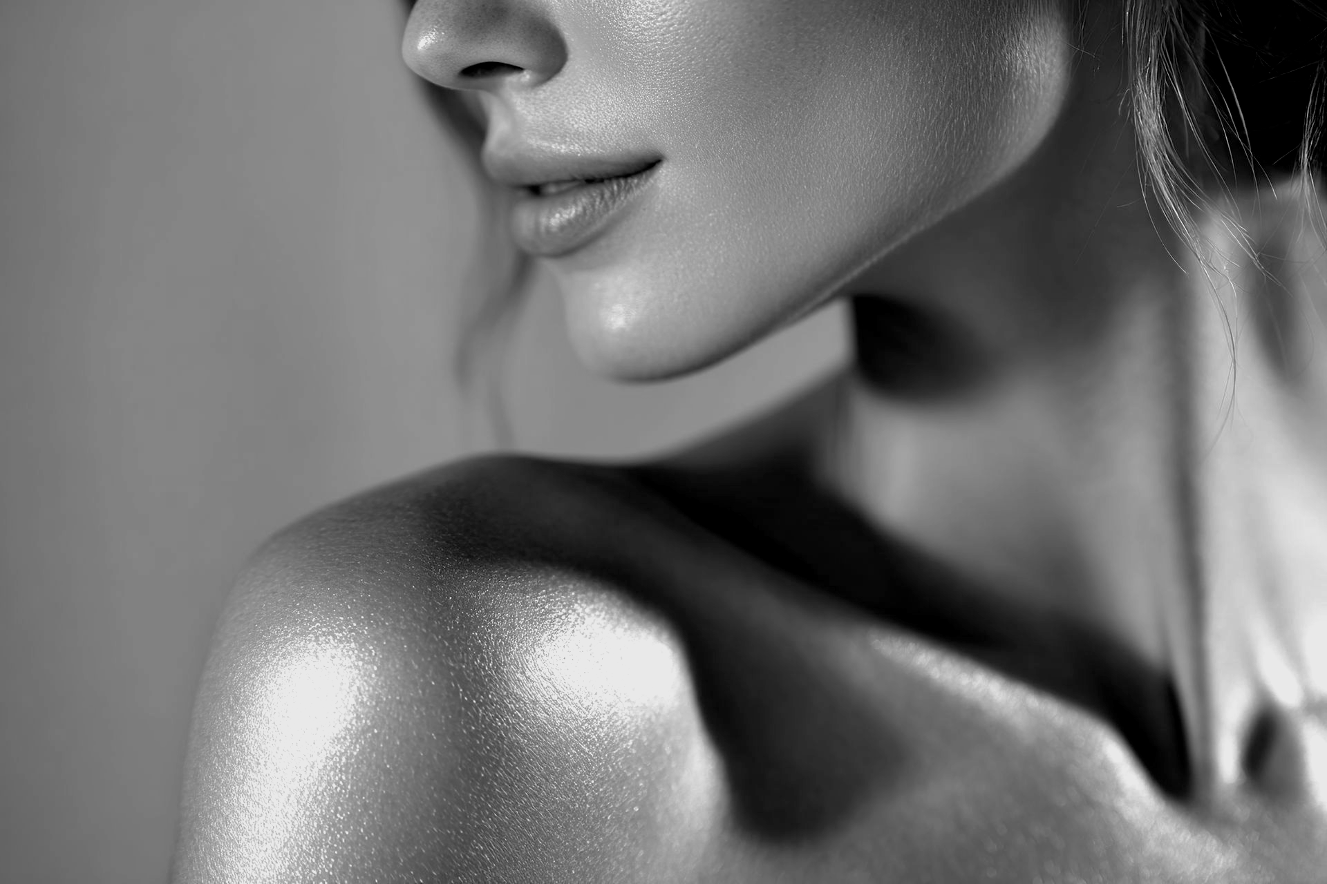 Gros plan en noir et blanc d'une peau éclatante sur une épaule, un cou et le bas du visage, avec une texture radieuse et rosée.