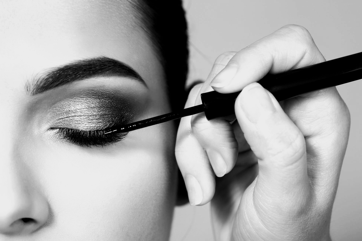 Gros plan en noir et blanc d'une personne appliquant un eye-liner liquide sur sa paupière.