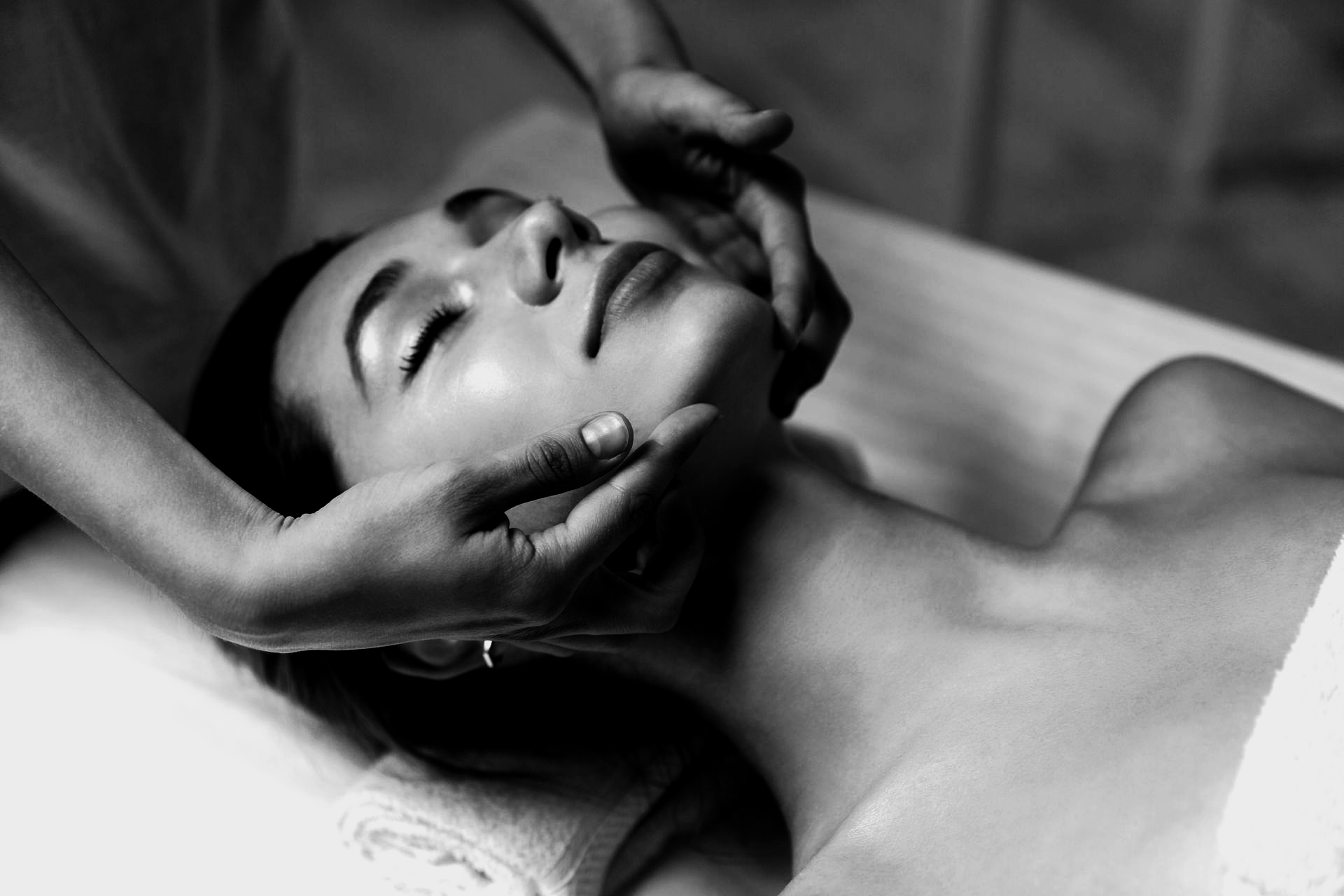 Une personne reçoit un massage facial relaxant, allongée dans un spa ; la scène est photographiée en noir et blanc.