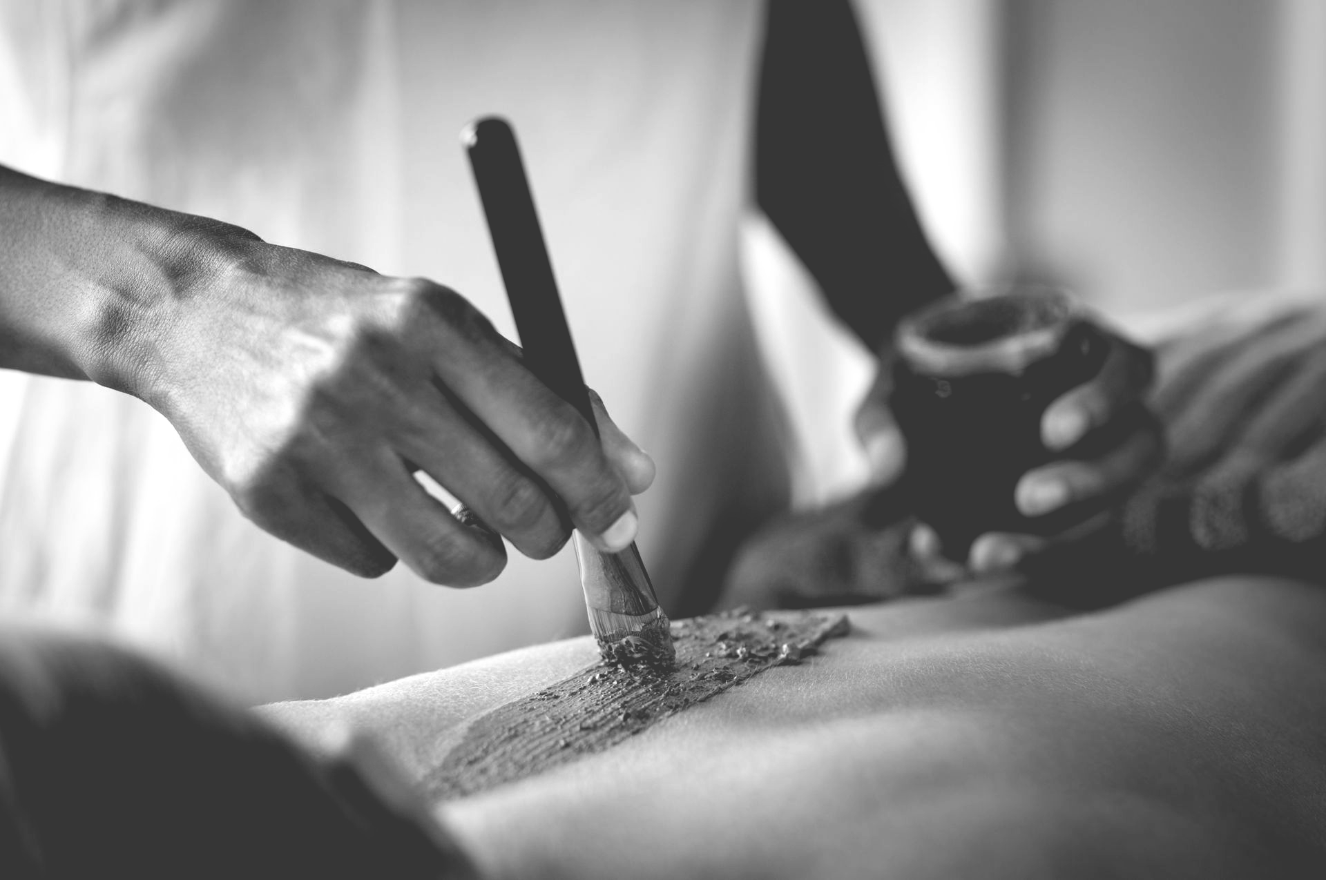 Dans un spa, une personne applique un masque ou un soin du visage sur le dos d'une autre personne à l'aide d'un pinceau.