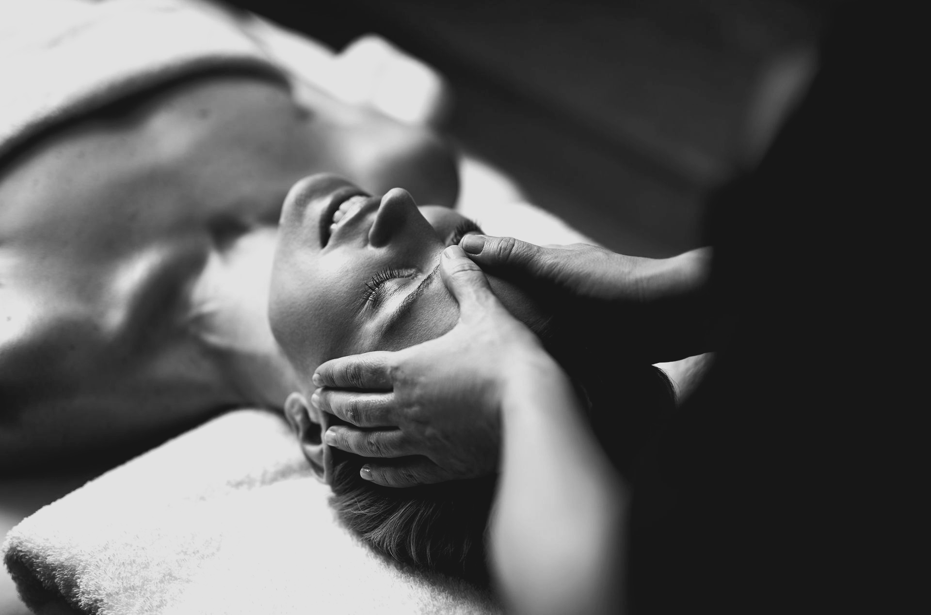 Gros plan en noir et blanc d'une personne allongée sur une serviette pendant qu'elle reçoit un massage facial relaxant.