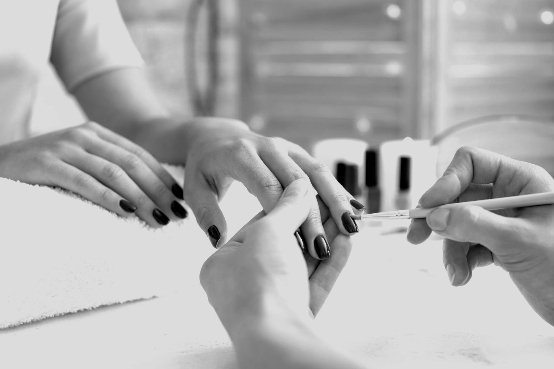Dans un salon de beauté, une technicienne en onglerie utilise un petit outil pour soigner avec précision les ongles vernis d'une cliente.