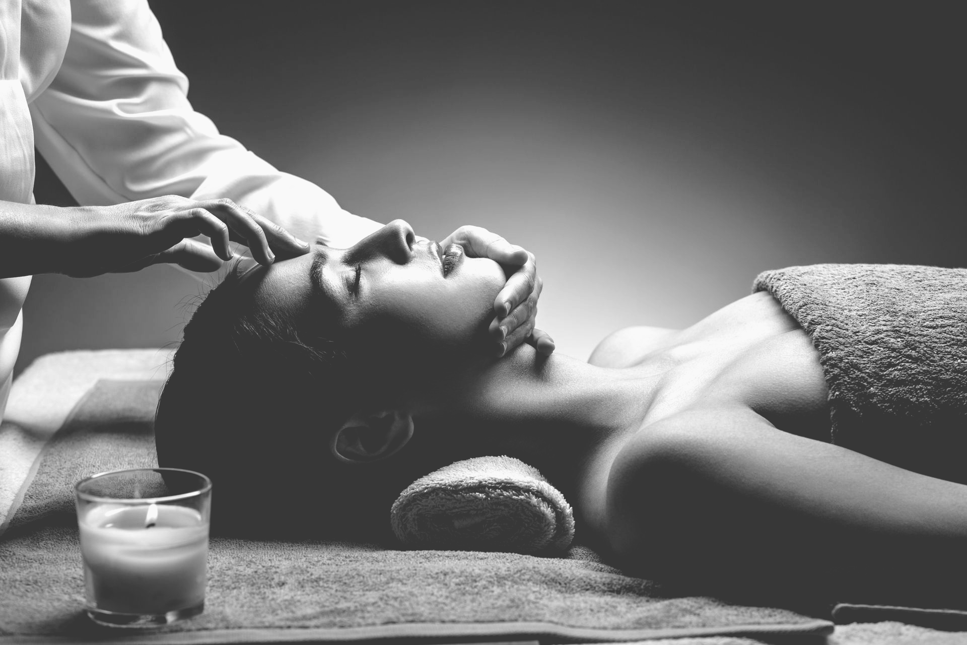 Une personne reçoit un massage facial relaxant dans un spa à l'éclairage tamisé, avec une bougie allumée au premier plan.