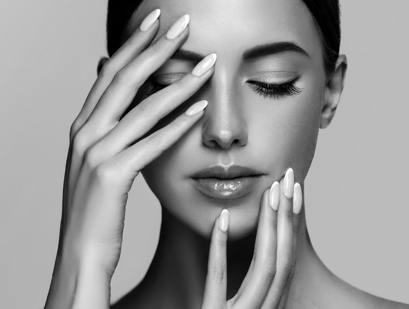 Portrait en noir et blanc d'une personne aux yeux fermés, touchant délicatement son visage de ses mains manucurées.