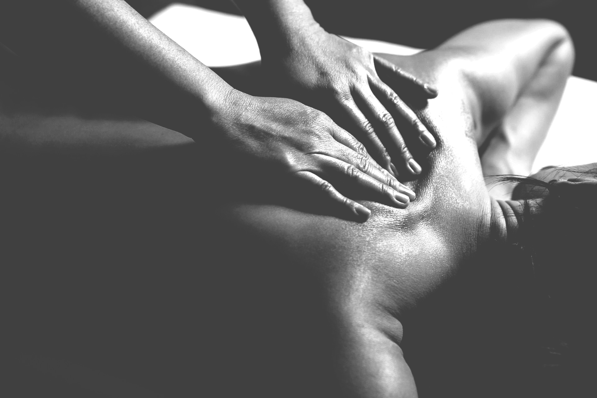 Une photo en noir et blanc montre des mains effectuant un massage thérapeutique du dos sur une personne allongée sur une table de massage.