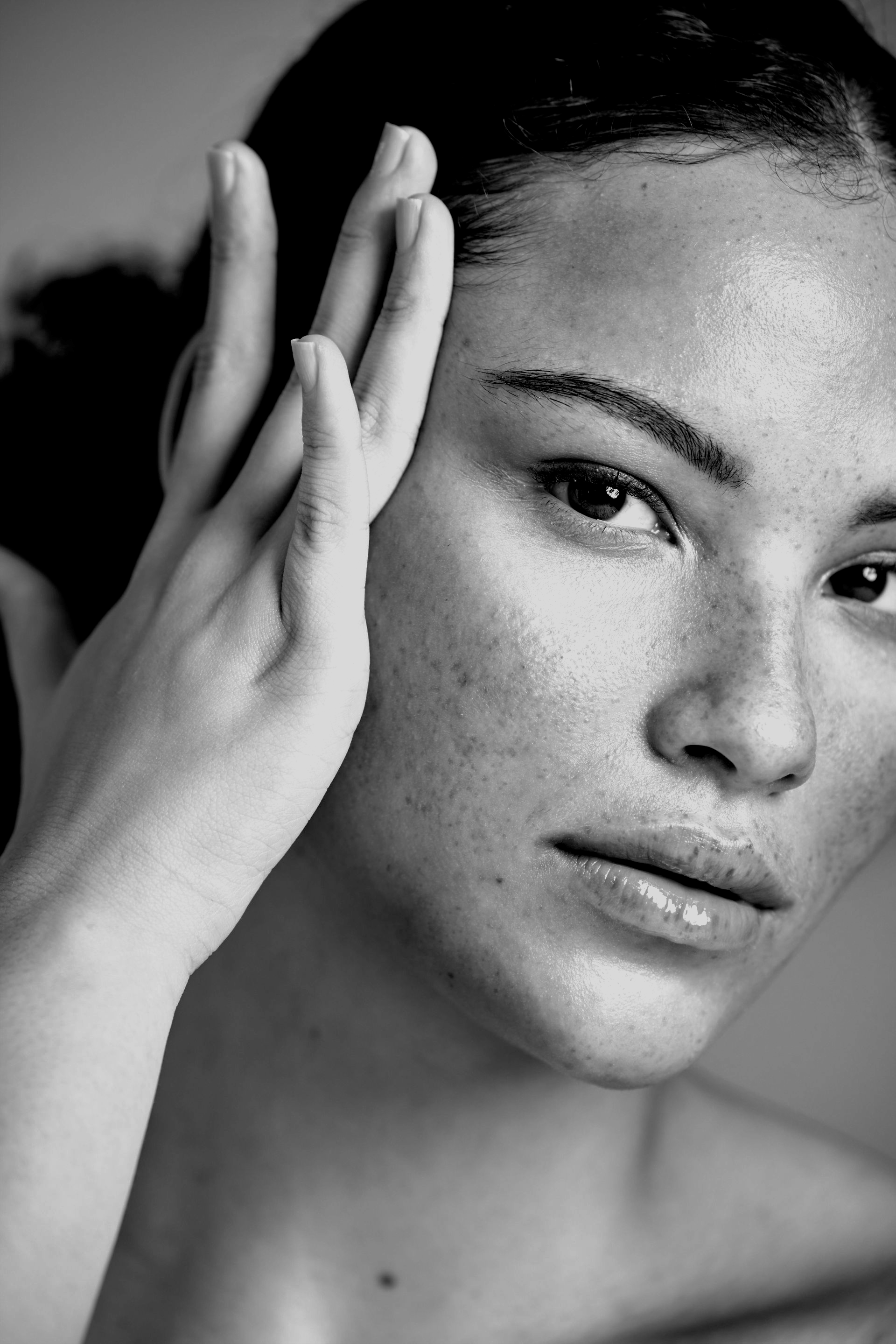 Gros plan en noir et blanc d'une personne se touchant le visage, regardant la caméra avec une expression neutre.