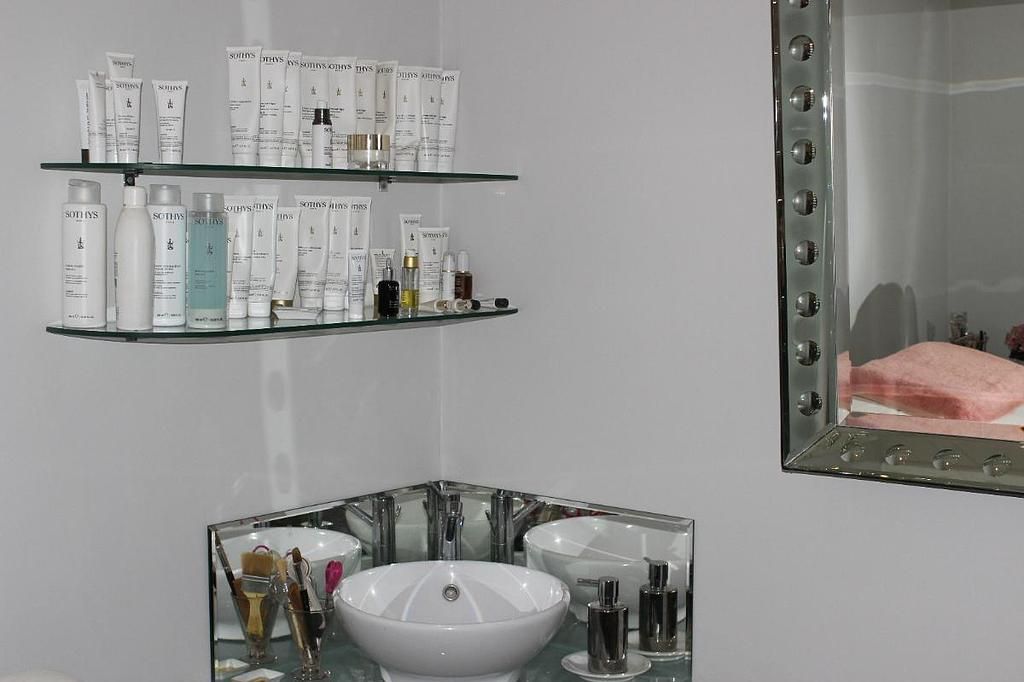 Meuble-lavabo de salle de bain avec étagères en verre pour les articles de toilette, un lavabo et un miroir reflétant une serviette rose.