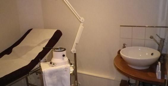 Salle de massage avec table de soins, lampe réglable et lavabo sur support en bois.