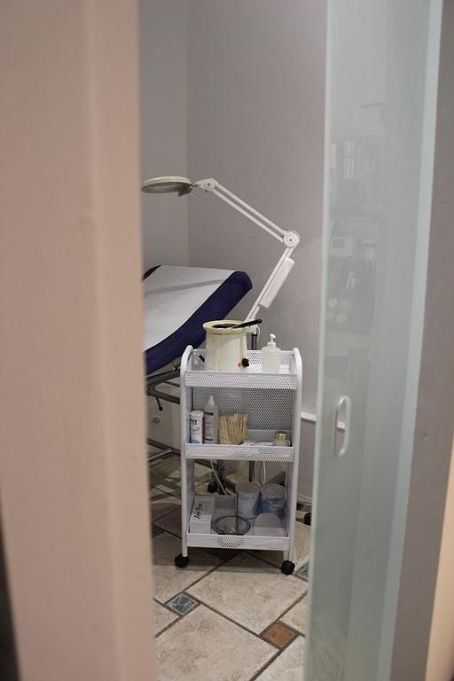 Salle médicale avec table d'examen et chariot à lampes sur roulettes dans l'embrasure d'une porte, visible à travers une porte entrouverte.