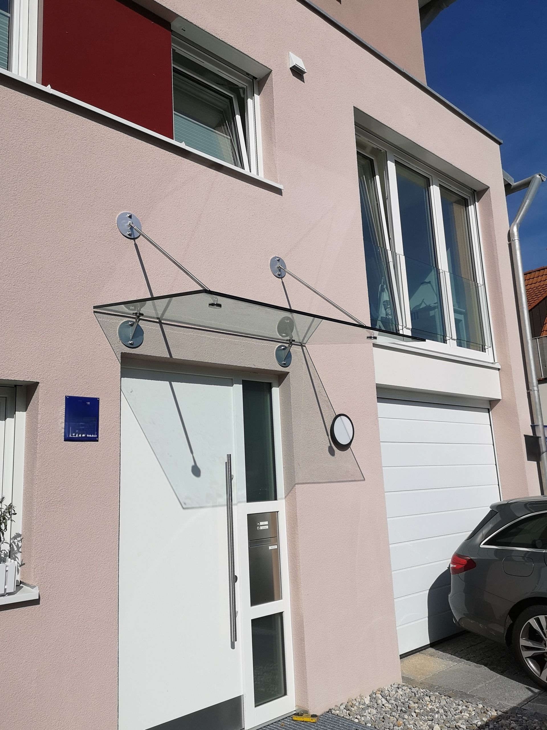 Glasvordach mit Edelstahlhaltern über einer Hauseingangstür.