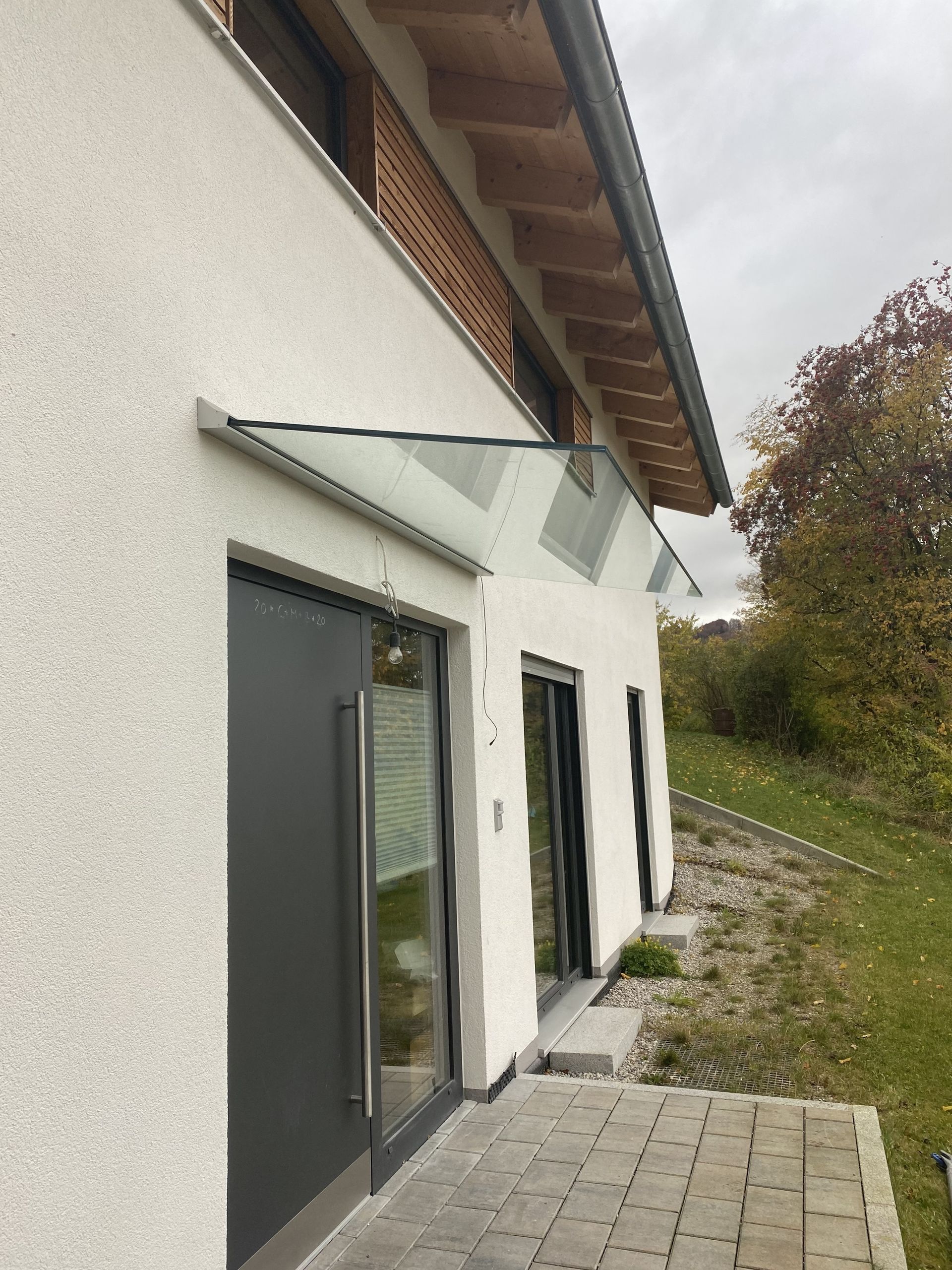Glasvordach mit Edelstahlhaltern über einer Hauseingangstür.