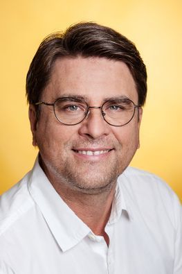 Mann mit Brille lächelt, trägt ein weißes Hemd.