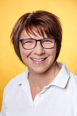 Frau mit kurzen braunen Haaren und Brille lächelt.