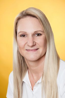 Frau mit blonden Haaren lächelt in einem weißen Hemd.