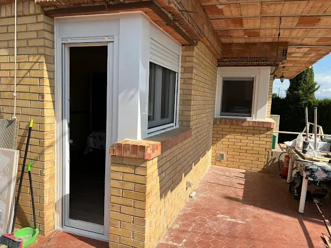 Exterior de un edificio con fachada de ladrillo, molduras blancas alrededor de una puerta y una ventana. Se ve un porche.