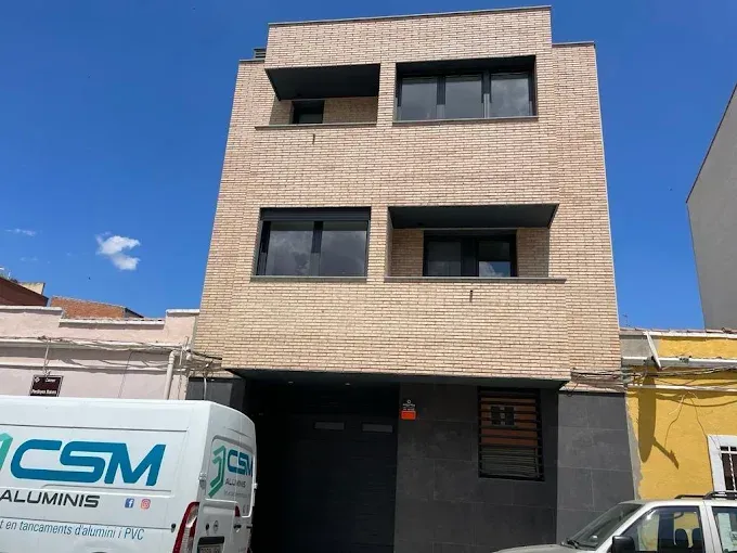 Edificio de ladrillo con ventanas oscuras que ocultan parcialmente una furgoneta con el logotipo de CSM Aluminis.