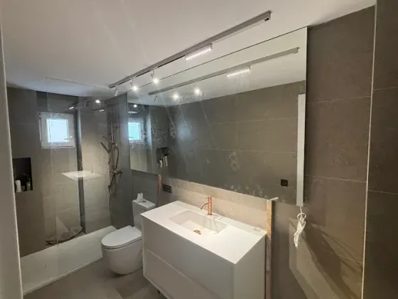 Baño moderno con paredes grises, tocador blanco, espejo grande y riel de iluminación.