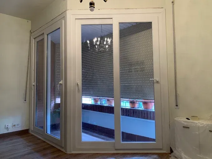 Puerta de vidrio con marco blanco y persianas que da a un balcón. Fotografía interior de una habitación.