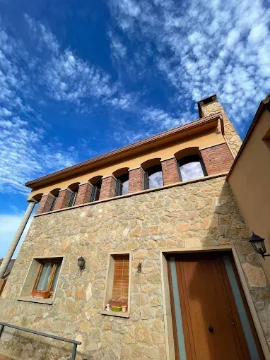 Casa de piedra con puerta marrón, detalles de ladrillo y cielo azul con nubes.