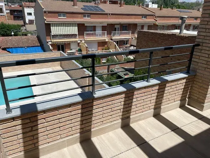 Balcón de ladrillo con barandilla metálica con vistas a zona residencial y piscina.