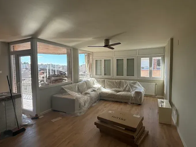 Sala de estar con sofá revestido de plástico, grandes ventanales y ventilador de techo.