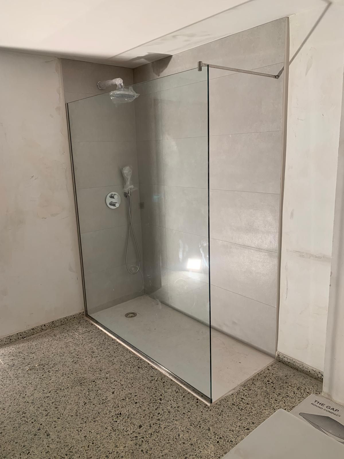 Cabina de ducha con paredes de cristal y azulejos grises.