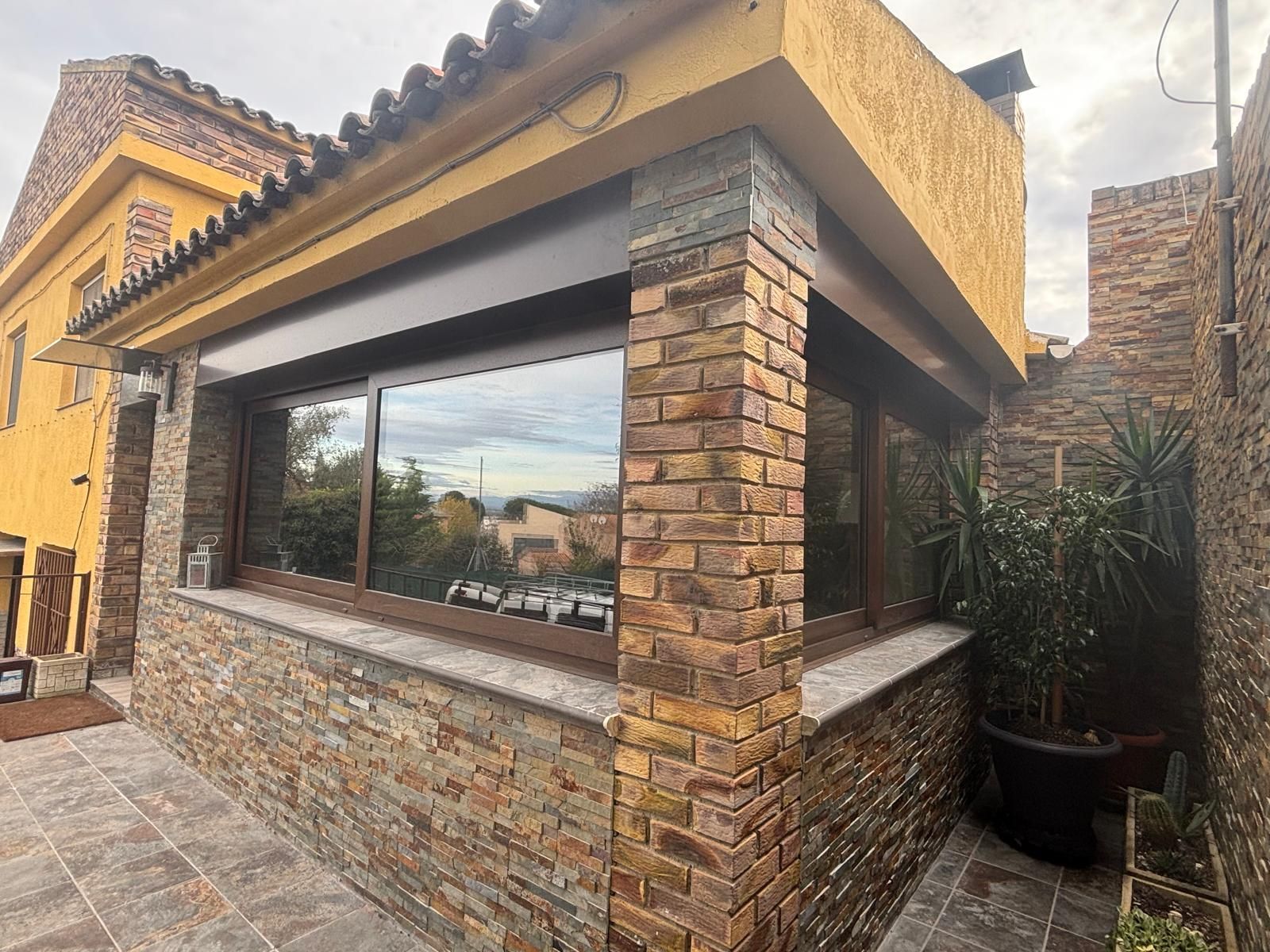 Edificio con exterior de piedra y ladrillo, grandes ventanales, molduras marrones y planta en maceta.