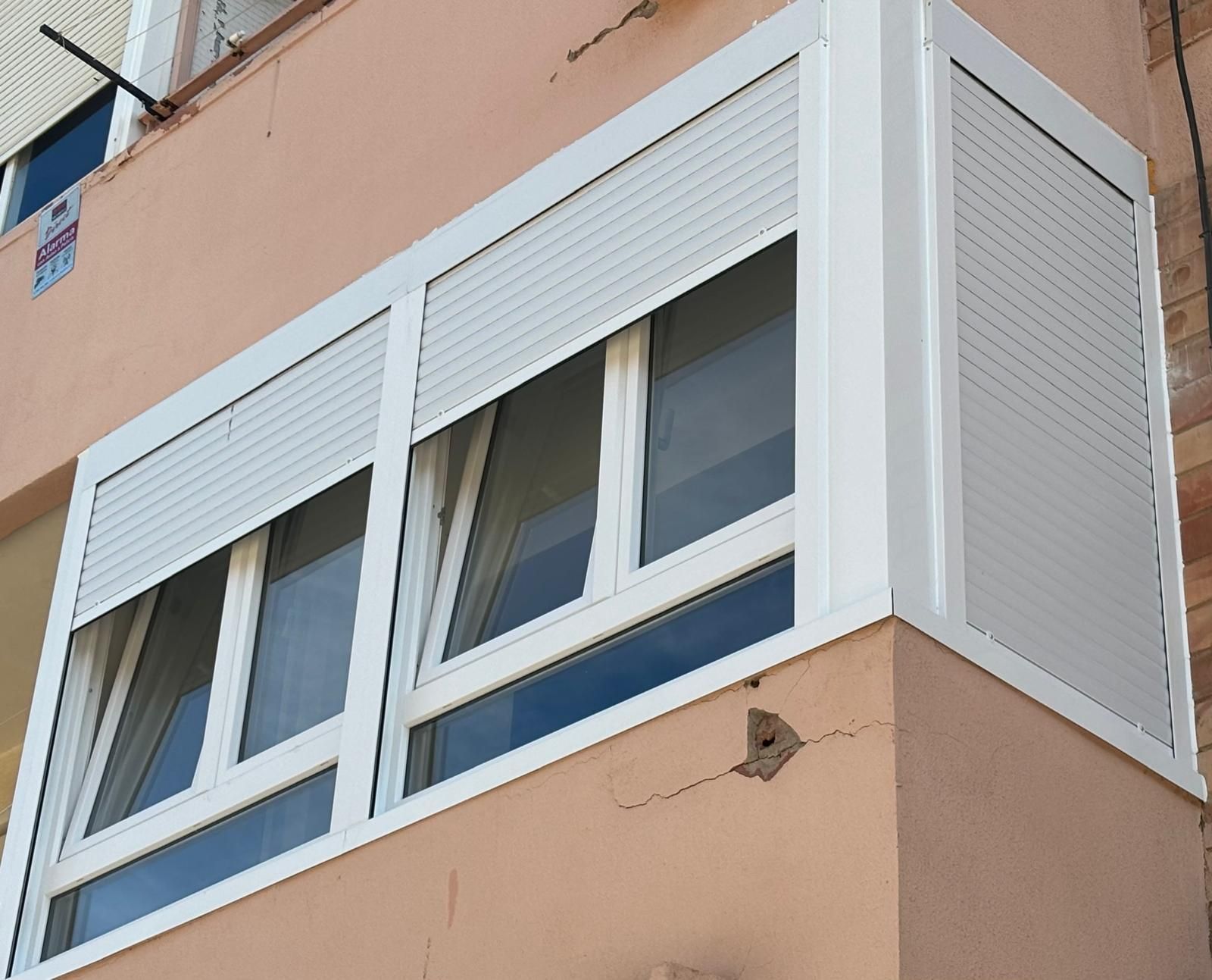 Ventanas con contraventanas blancas en la esquina de un edificio de color canela.