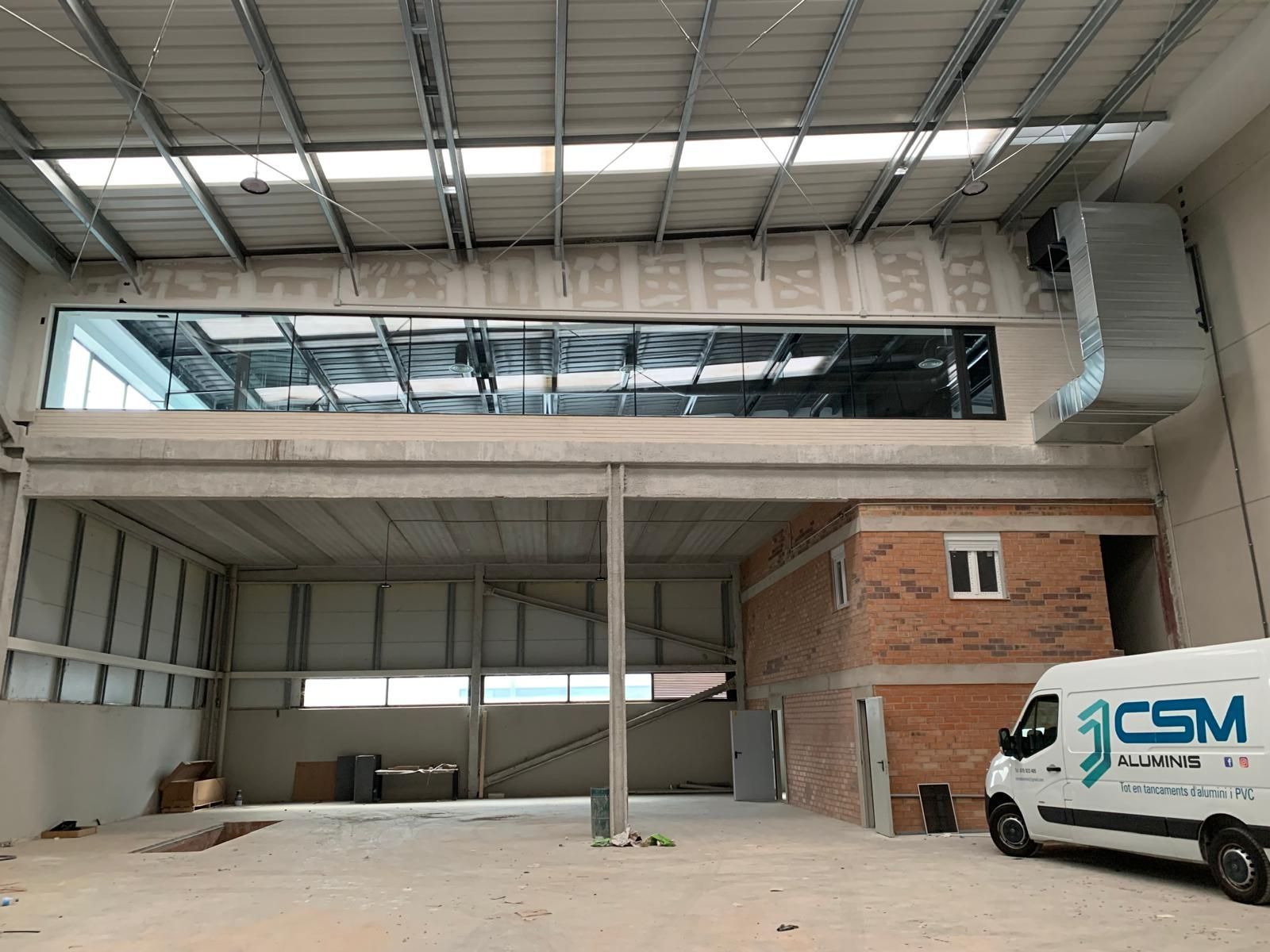 Interior de una nave industrial en construcción, con entrepiso. Cuenta con techo visto, paredes de ladrillo y furgoneta.