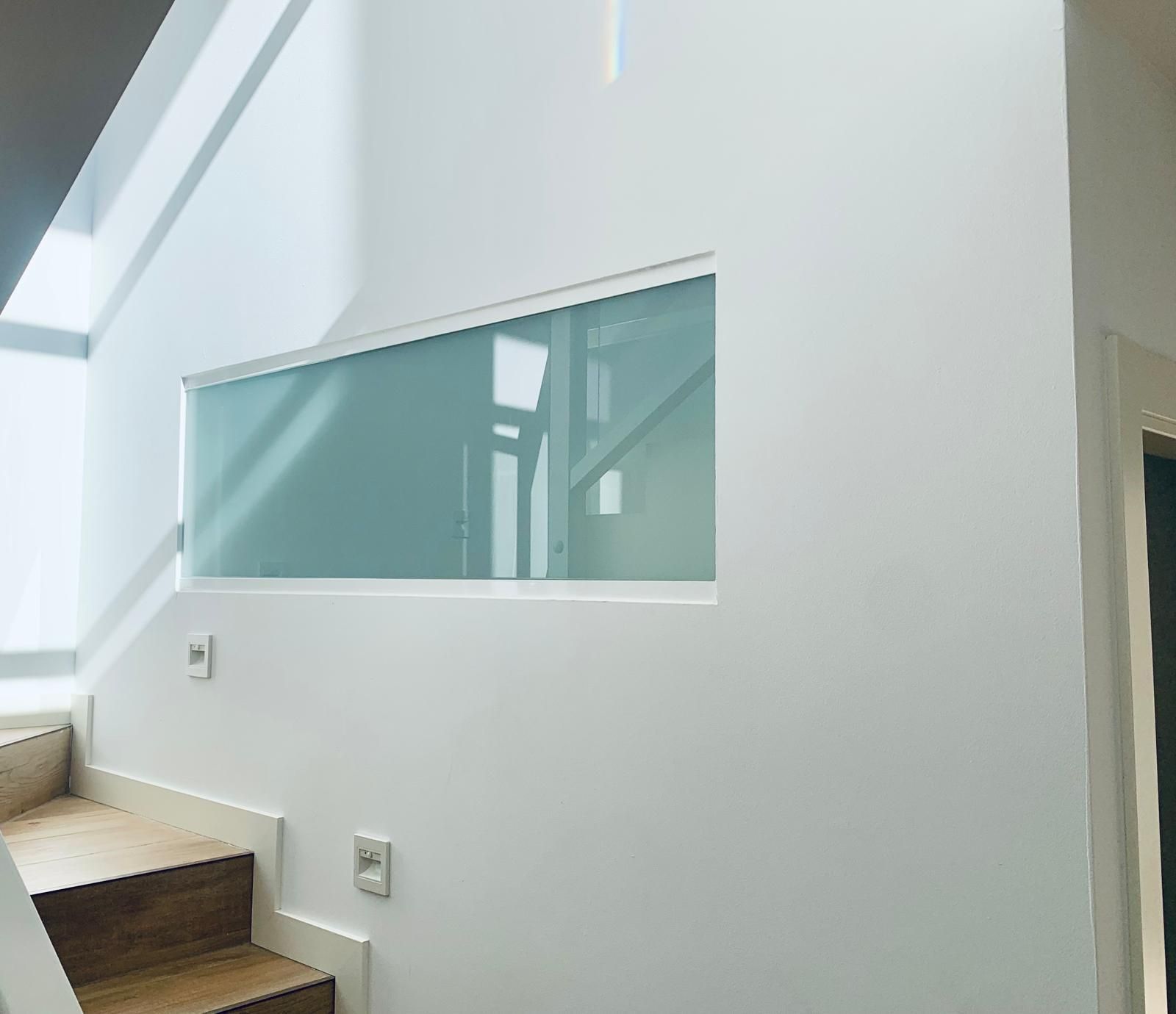 Escalera con escalones de madera y paredes blancas. Ventana rectangular con vidrio esmerilado.