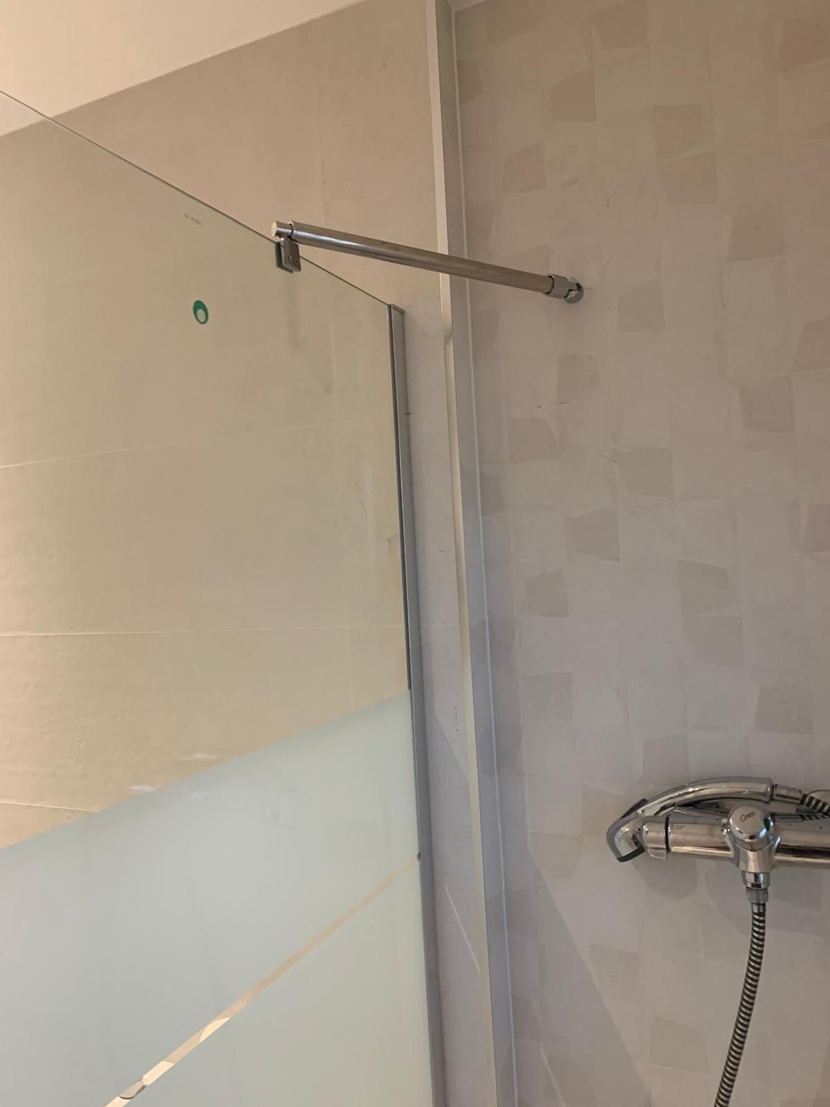 Ducha con puerta de cristal, herrajes cromados y cabezal de ducha.