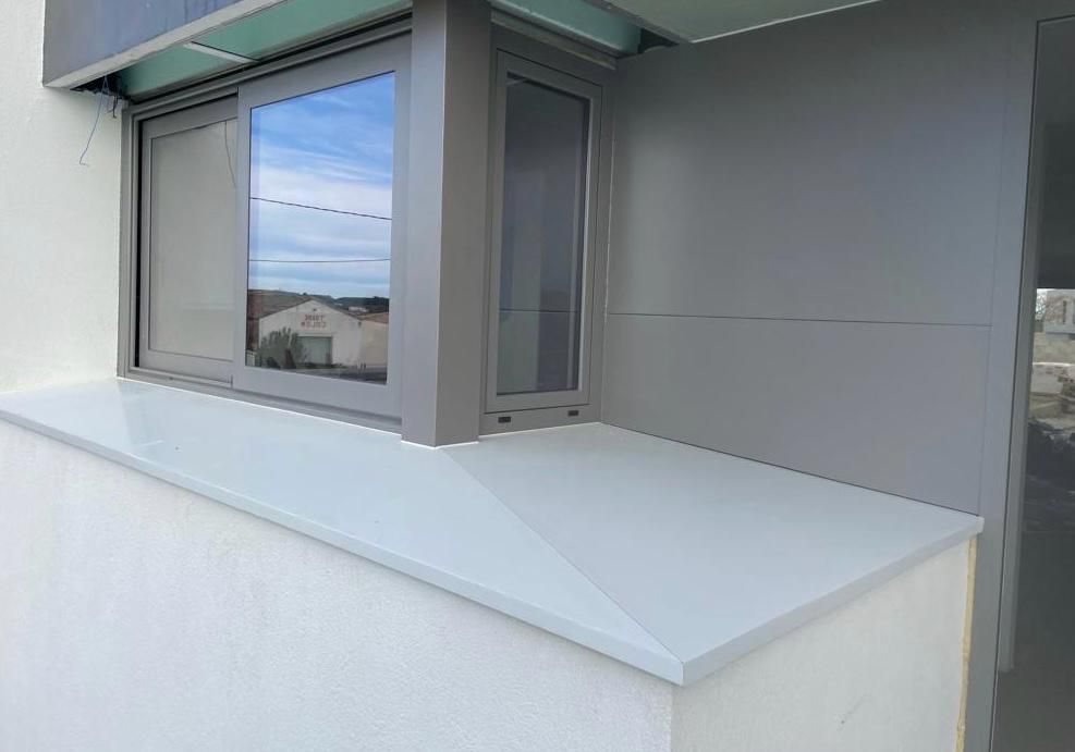 Ventana gris en un edificio blanco con un alféizar de ventana gris, que refleja un cielo azul.