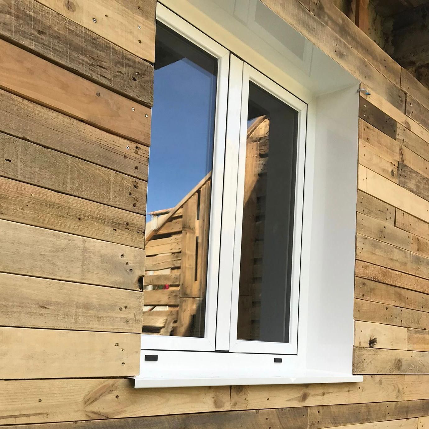 Ventana con marco blanco en un edificio de madera. Reflejo de una valla en el cristal.