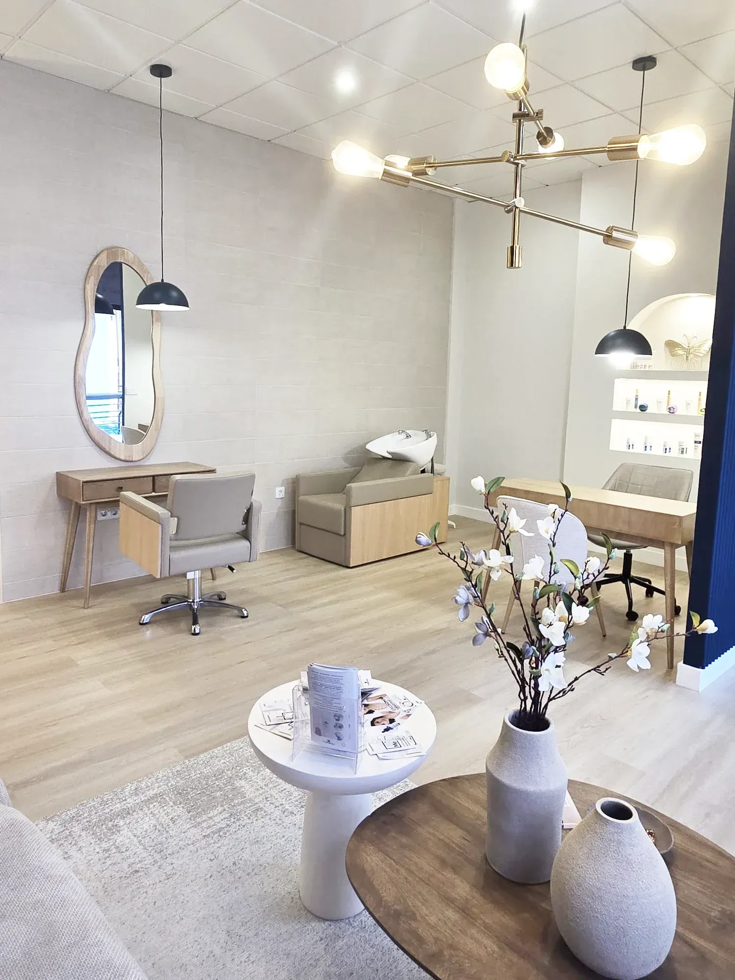 Interior del salón: tonos neutros, detalles en madera, estación de peluquería, estación de uñas, asiento.