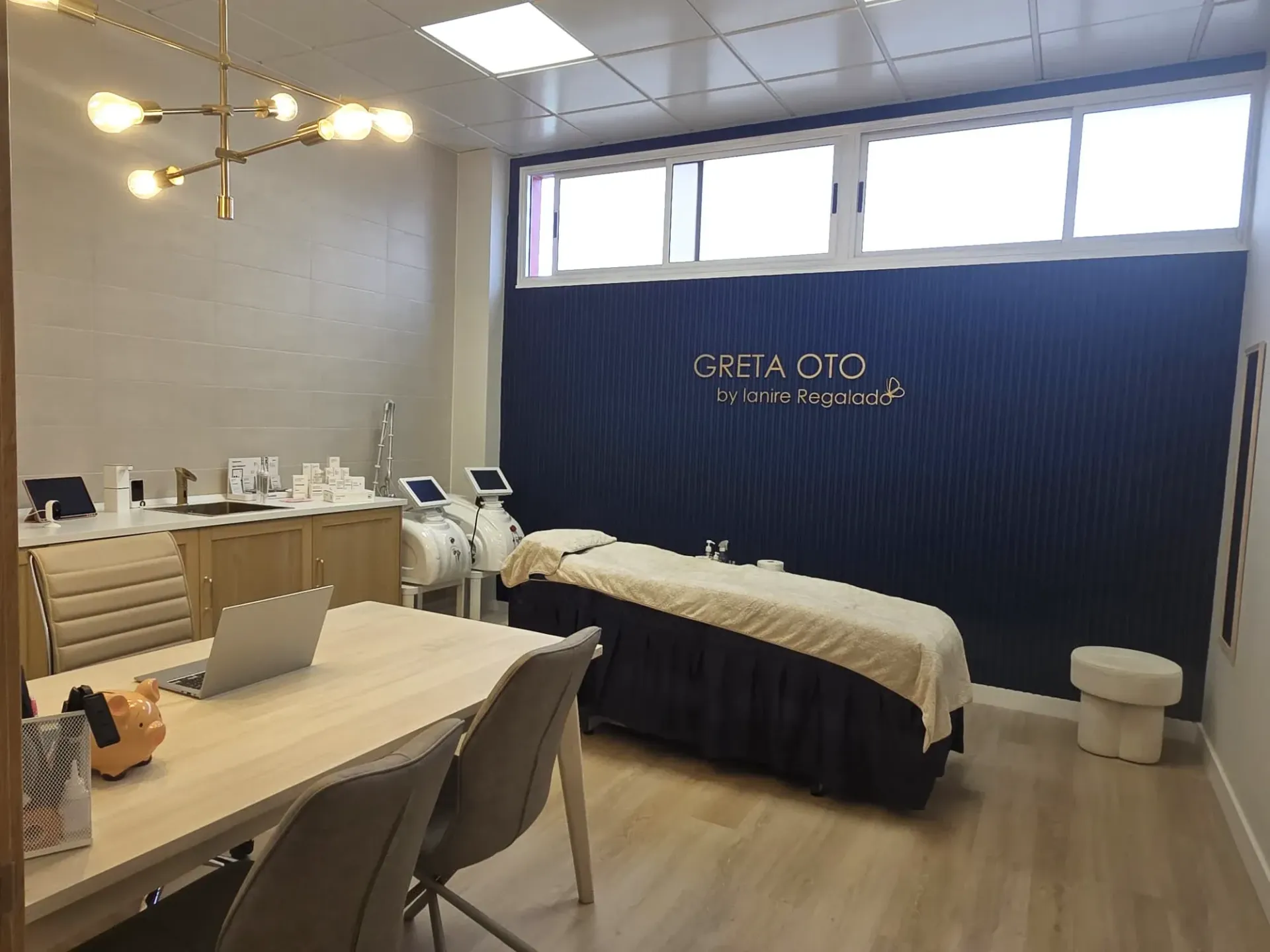 Sala de tratamiento de spa médico con cama, equipo, escritorio y logotipo dorado sobre fondo negro.