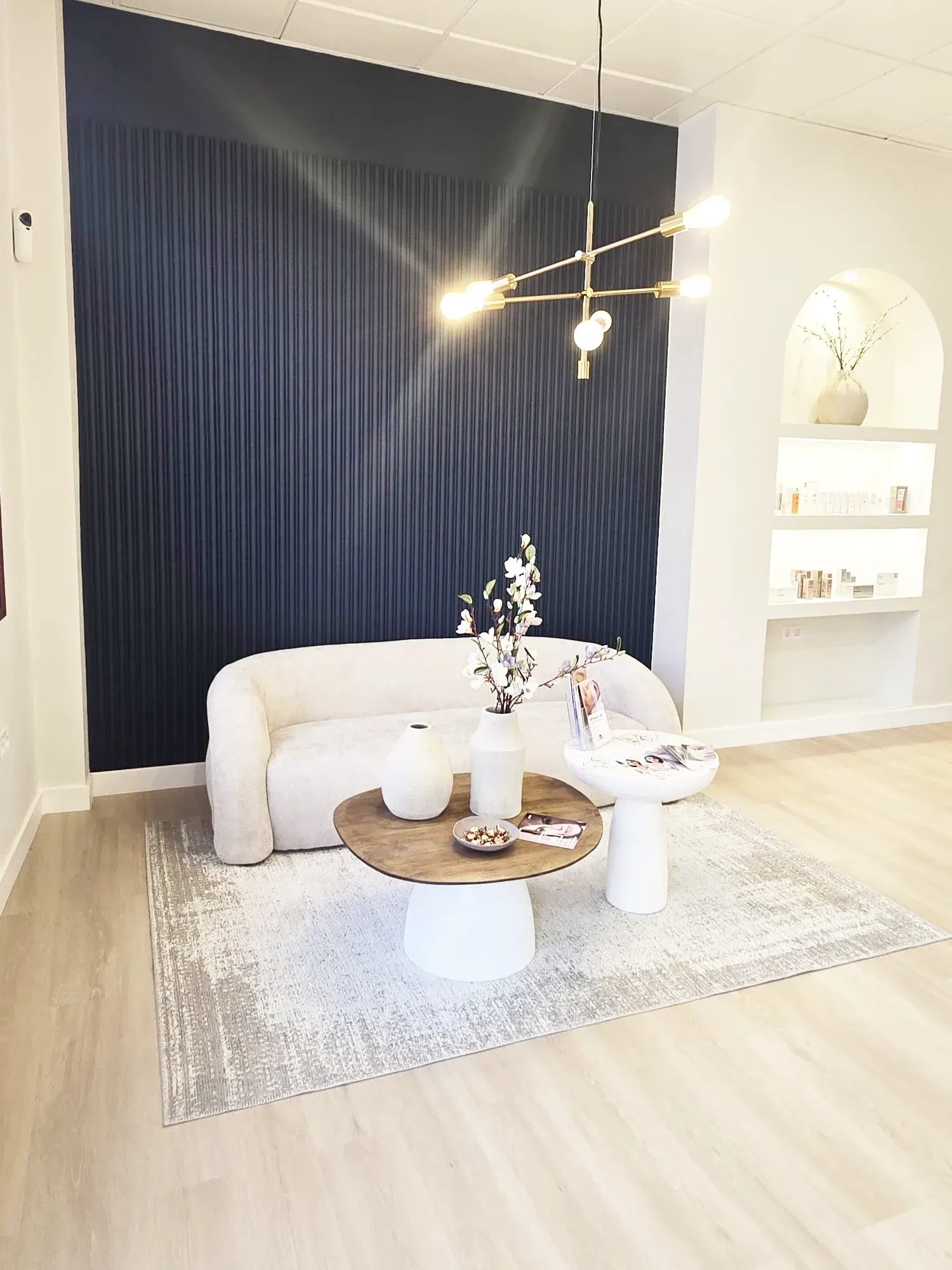 Acogedor salón con pared texturizada azul, sofá crema, mesas redondas y lámpara de araña moderna.