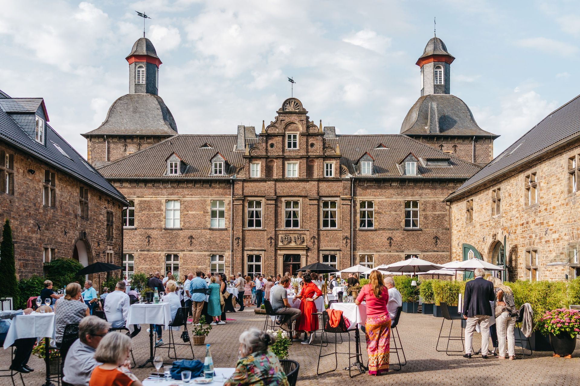 Der Innenhof im Schlosshotel Hugenpoet  in Essen bei einem Event mit zahlreichen Gästen und sommerlichem Wetter.