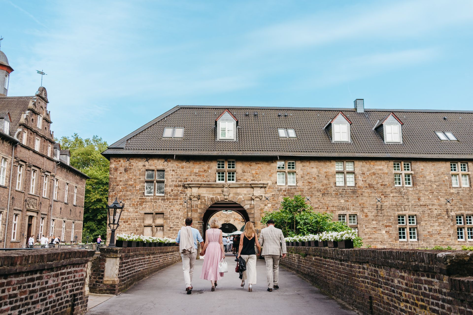 Vier Gäste, die bei strahlendem Sonnenschein die Auffahrt zum Schloss Hugenpoet in Essen hochlaufen.