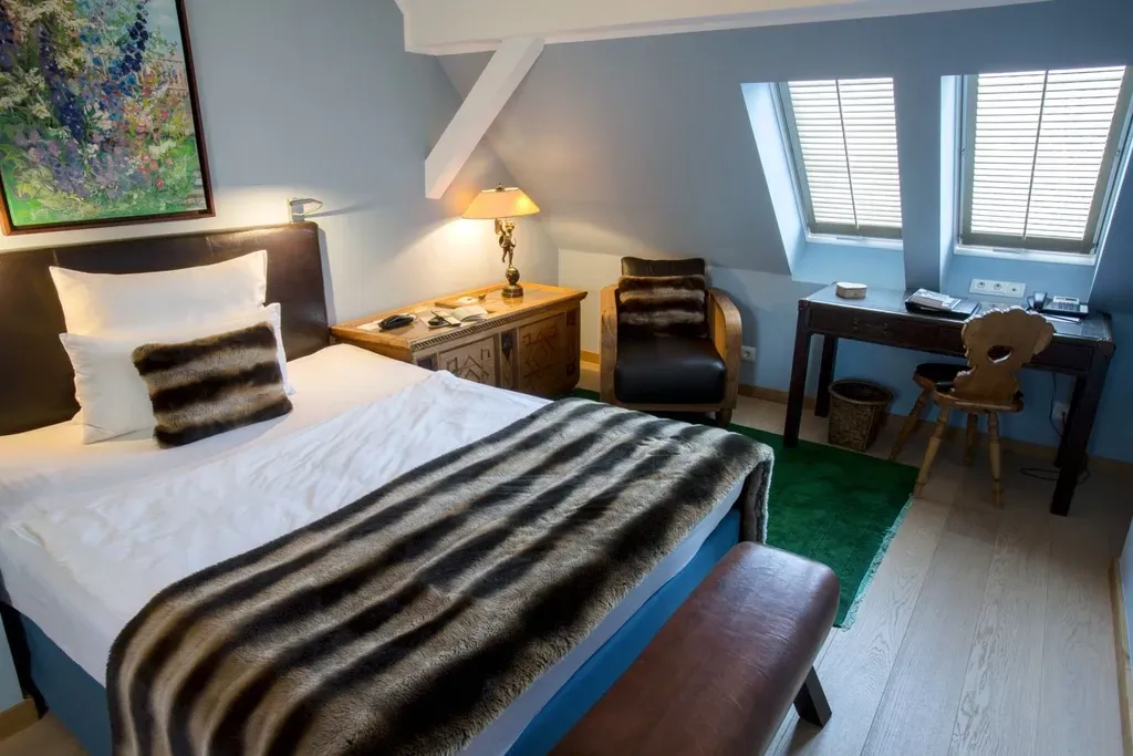 Ein Hotelzimmer mit einem Bett, einem Schreibtisch, Stühlen und einem Gemälde an der Wand im Schlosshotel Hugenpoet in Essen.