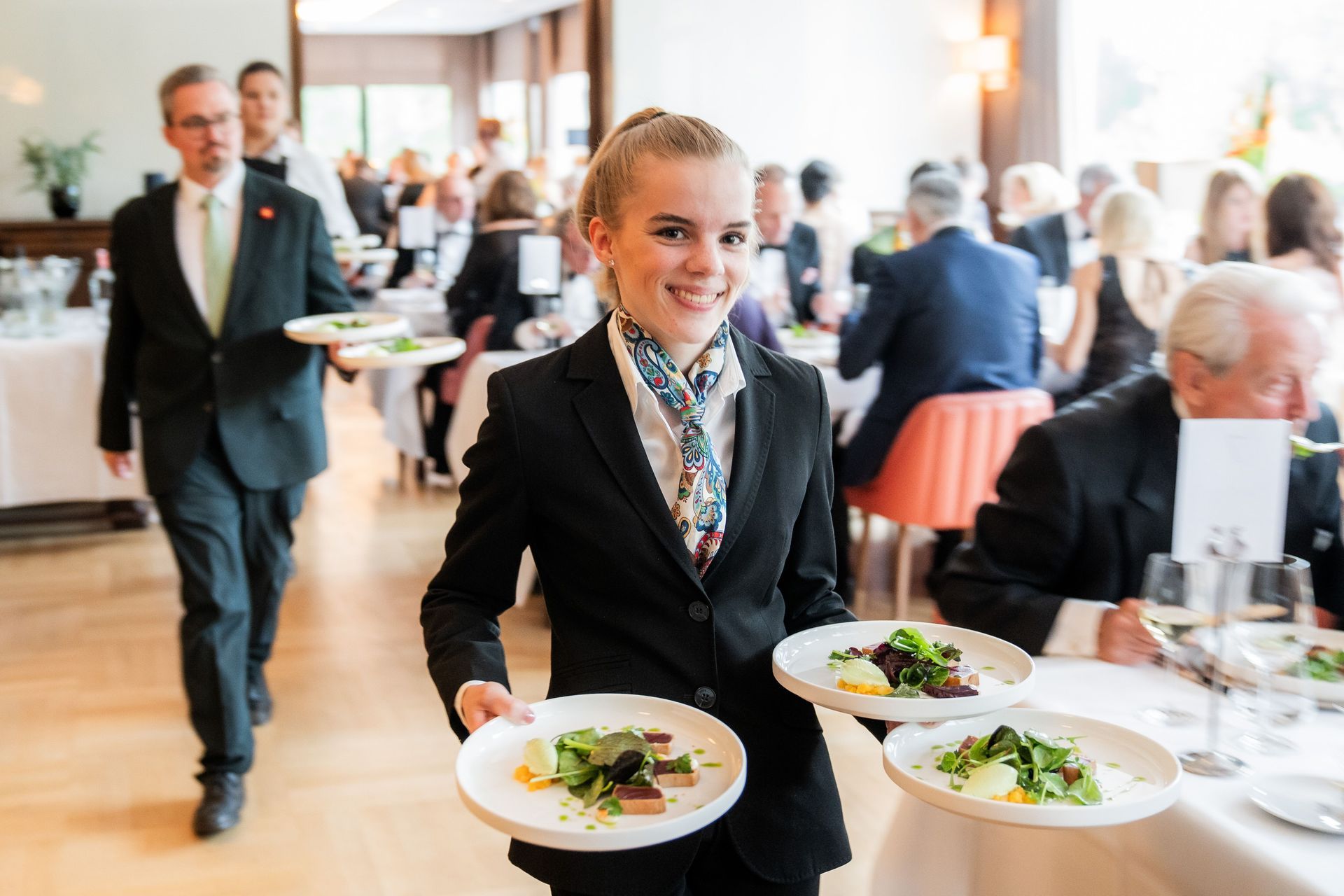 Eine Auszubildende serviert drei Teller bei einer Veranstaltung im Schlosshotel Hugenpoet.