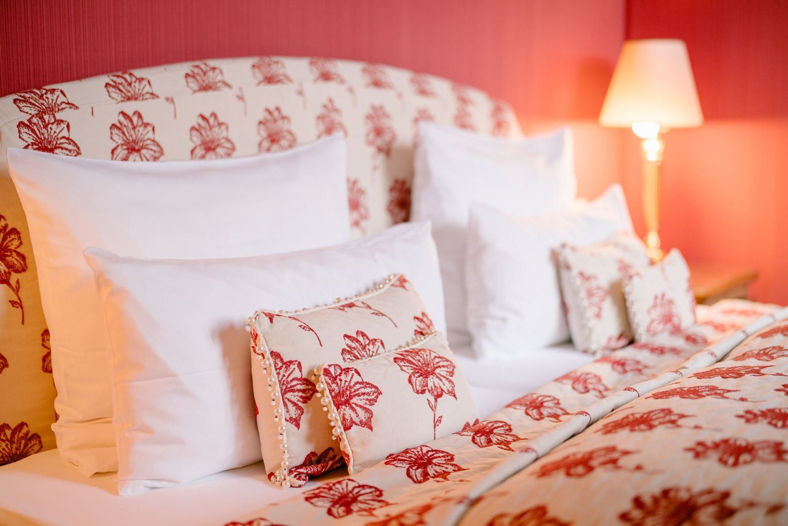 Ein Bett mit rot-weißer Bettwäsche und Kissen in einer Juniorsuite im Schlosshotel Hugenpoet in Essen.