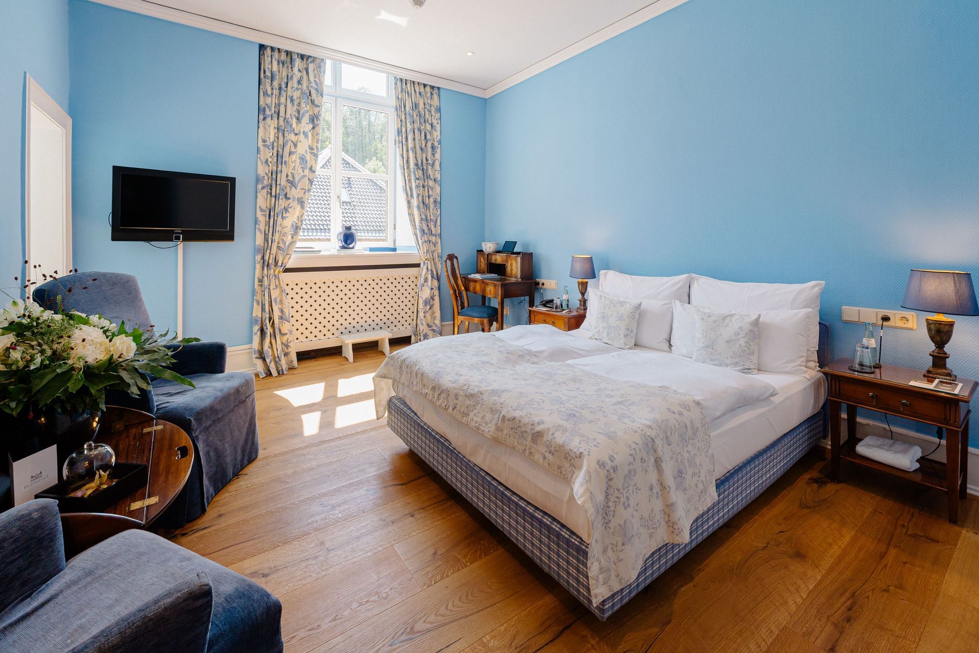 Ein gemütliches Classic Doppelzimmer mit blauen Wänden und modernem Parkettbogen im Schlosshotel Hugenpoet in Essen.