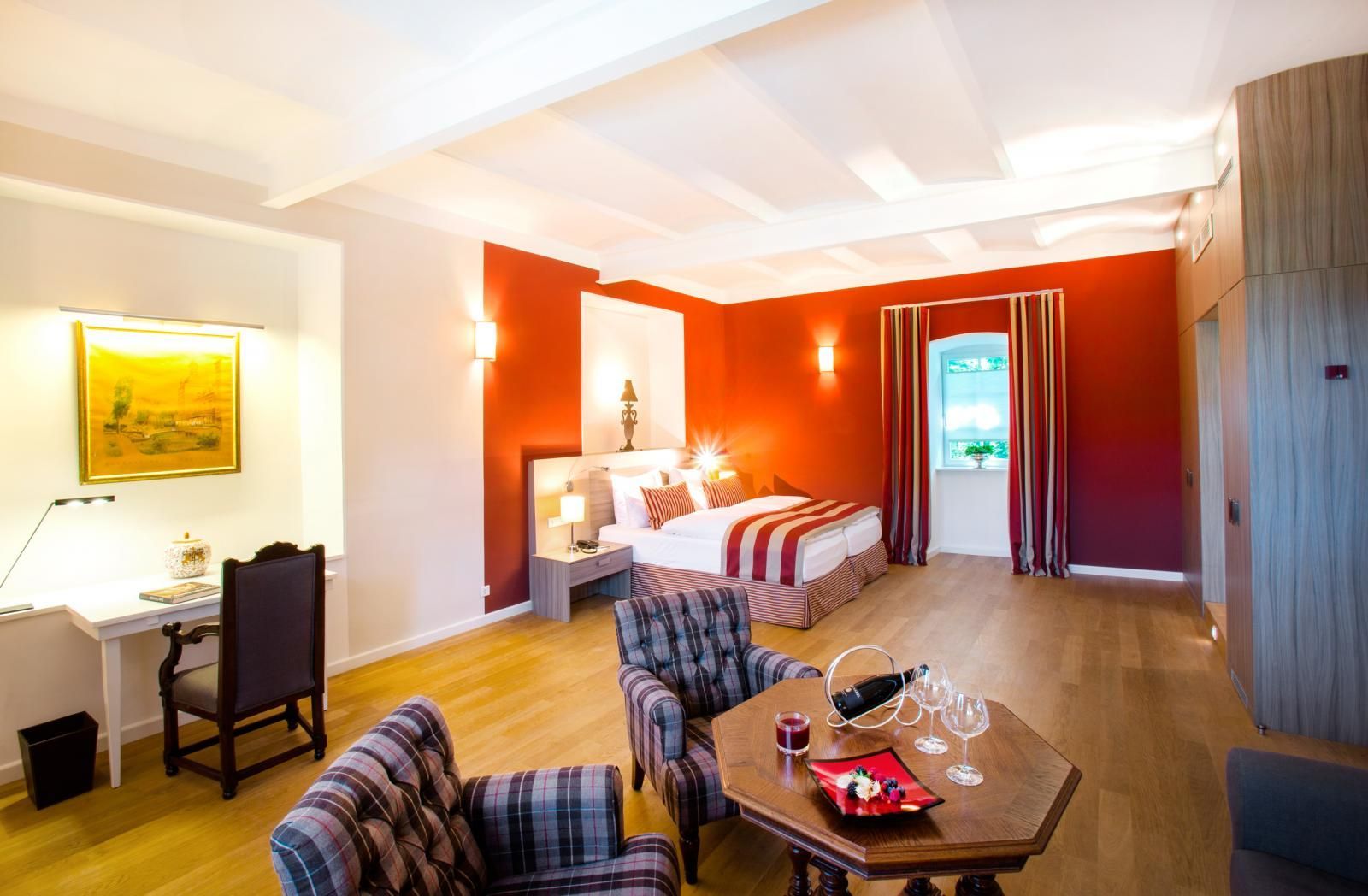 Der Wohn- und Schlafbereich einer geräumigen Juniorsuite mit roten Akzenten, einem Doppelbett und separater Sitzecke.