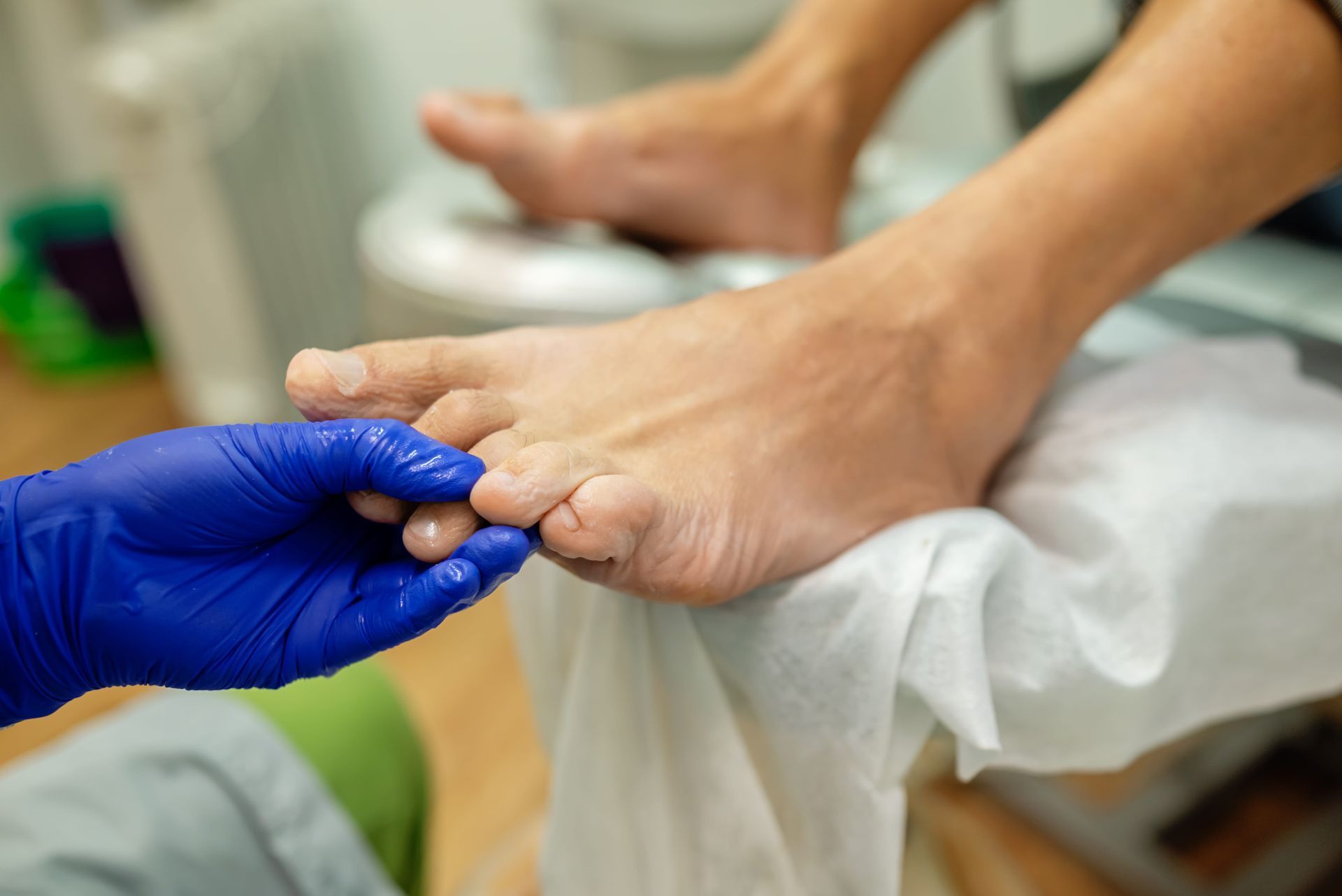 Manos enguantadas de azul limpiando el pie de una persona con un paño blanco en un entorno médico.
