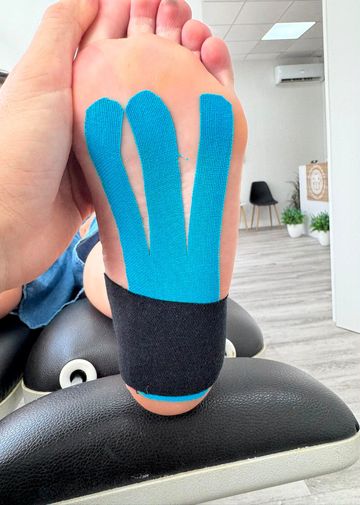 Un corredor, con zapatillas rojas, se estira en una pista de atletismo y extiende una mano hacia el suelo.