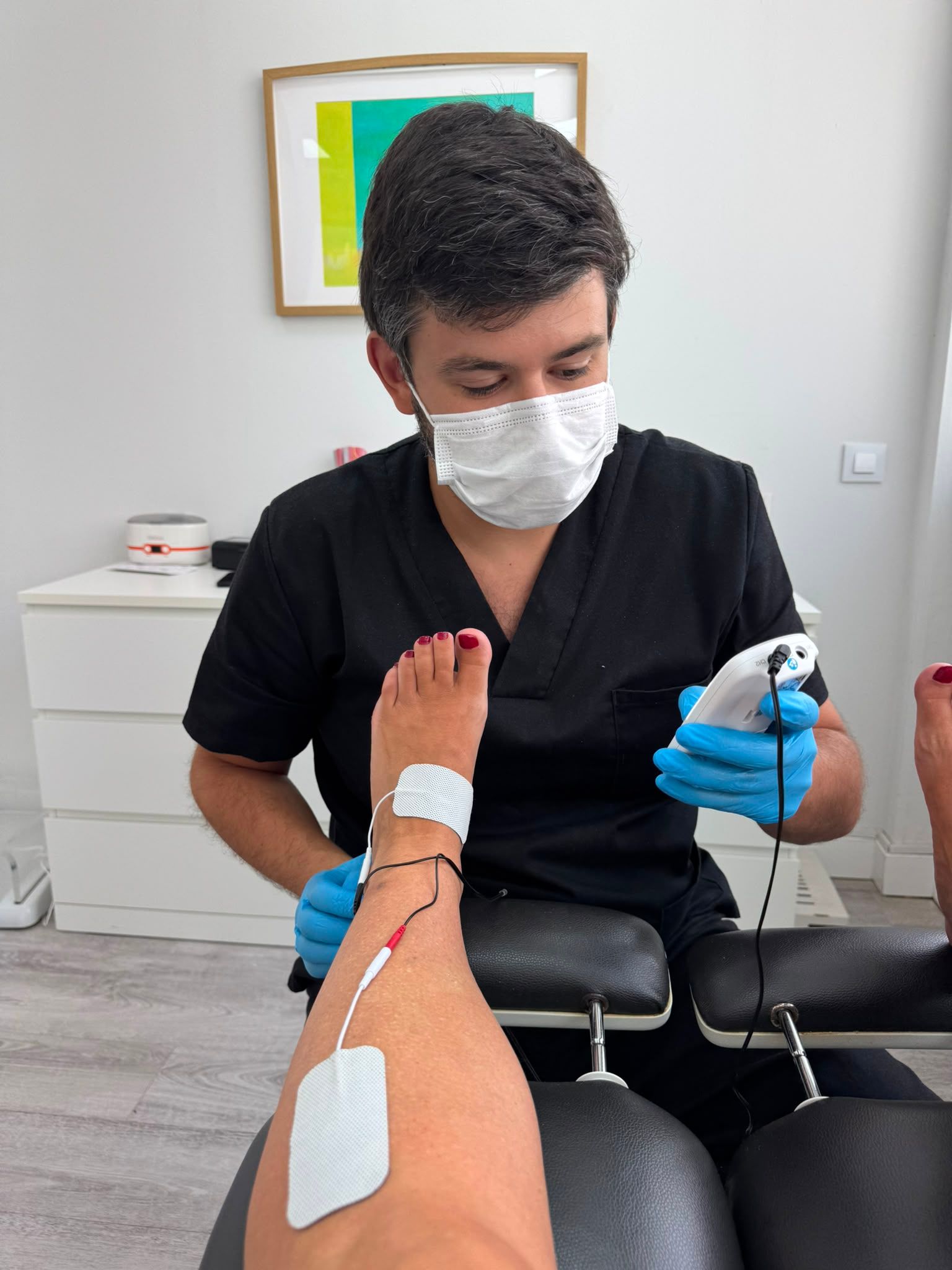 Masaje de pies en una clínica, donde un terapeuta con guantes y mascarilla facial atiende el pie de un paciente.