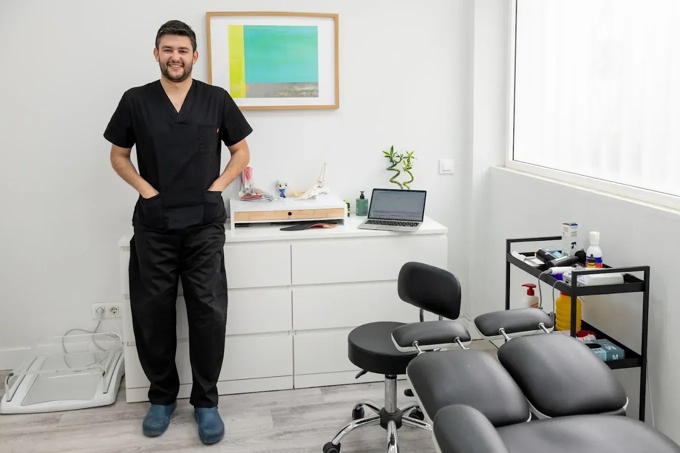 Hombre de pie en una luminosa sala de clínica con sillón de tratamiento y equipo médico.