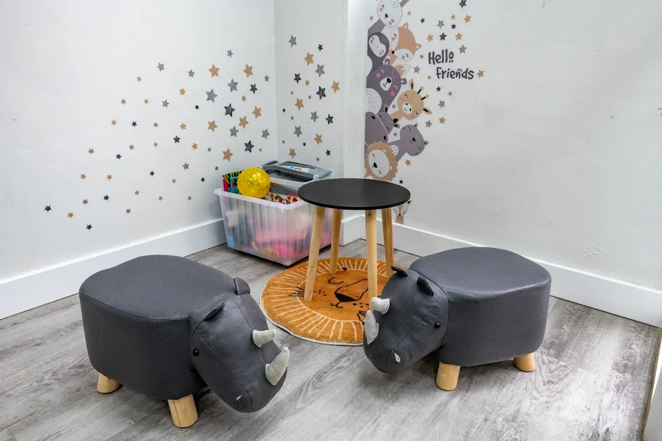 Dos taburetes grises con forma de hipopótamo junto a una pequeña mesa negra en un rincón de juegos infantil