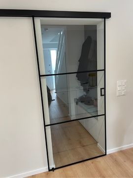 eine Schiebetür mit schwarzem Rahmen führt in einen Flur .