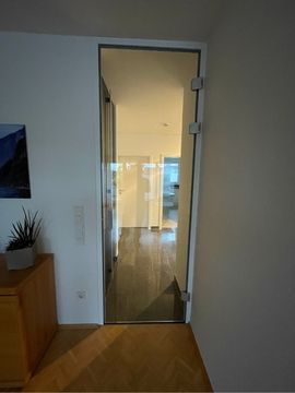 eine Glastür führt in ein Wohnzimmer mit Holzboden und weißen Wänden .